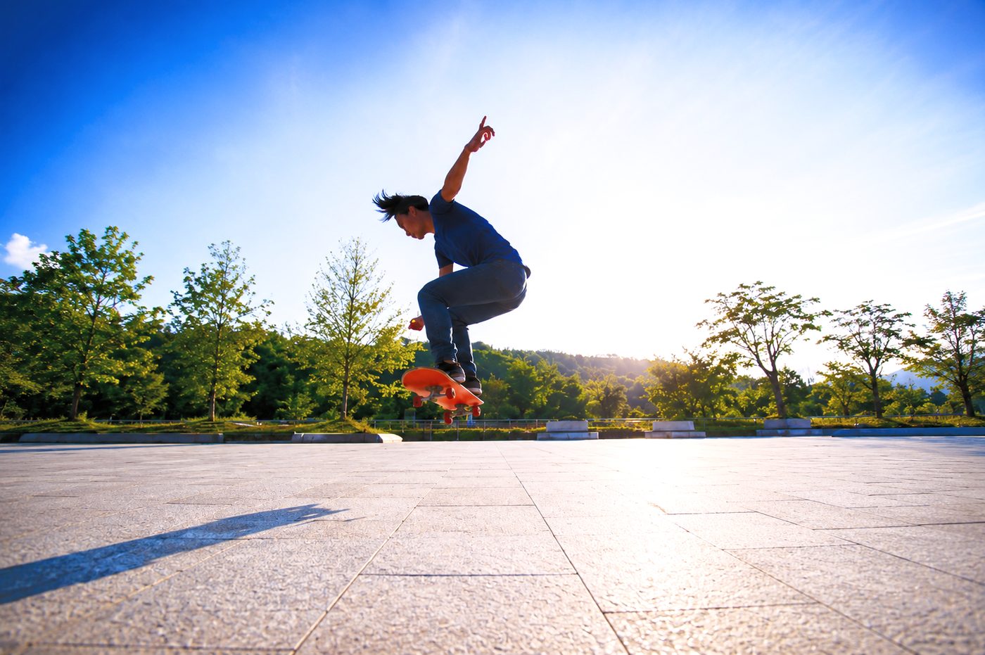 Silhouette d'un jeune homme en plein saut en skateboard dans un parc ensoleillé, symbolisant la liberté retrouvée grâce à l'hypnose.